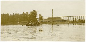 Horizontale, sepia foto van uniformeerde soldaten die een roeiboot over een groot overstroomd gebied peddelen door Carl Michel